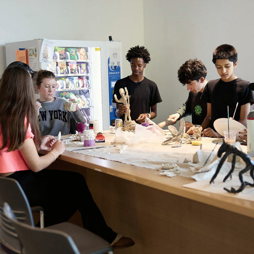 Students around a long table build sculptural prototypes from mixed materials.